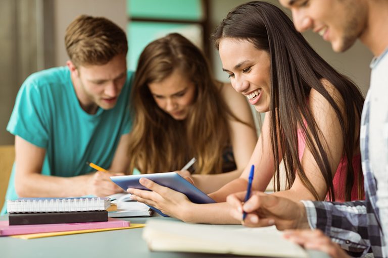 Smiling friends sitting studying and using tablet pc after school for teamwork